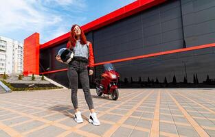 The Adventurous Woman and Her Bold Red Motorcycle. A woman standing in front of a red motorcycle photo