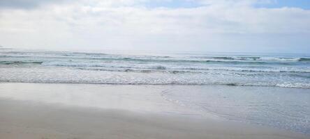 image of beach with white sand and calm sea on sunny day with bathers and surfers on the beach photo