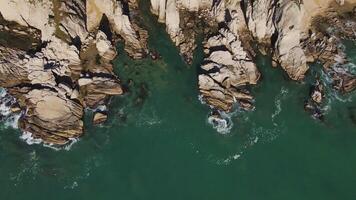 Wild rocky cliffs by sea aerial view by drone top view Cliffs bask bright sun sea's beauty beneath. Sea waves crash against cliffs nature's grandeur Majestic views untouched wilderness. video