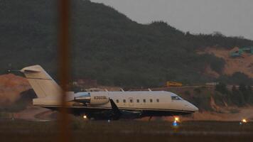 PHUKET, THAILAND - FEBRUARY 16, 2023. Private owner Bombardier Challenger 604, N360SL taxiing on the runway before takeoff, side view through the fence video