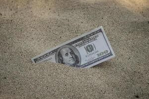 Paper currency 100 dollar bills partially buried in the sand photo