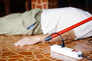 Using red plastic stick is moving away the electric plug socket from the unconscious man who lay down on the floor. Concept, Electric Shock. Emergency basic rescue. First Aid photo