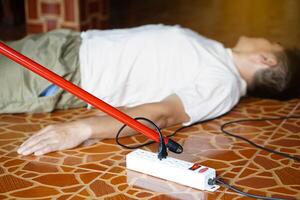 Using red plastic stick is moving away the electric plug socket from the unconscious man who lay down on the floor. Concept, Electric Shock. Emergency basic rescue. First Aid photo