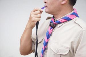 Close up man wears boy scout uniform is blowing the whistle. Concept, Scout blow whistle as meaningful sign for doing activity to assembly, start competition or playing games in scout lesson. photo