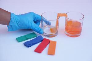 Hand wear blue glove, hold glass of color paper strip to absorb water to another glass. Concept, science lesson activity. Easy experiment for learning. Teaching education materials.  Learning design photo