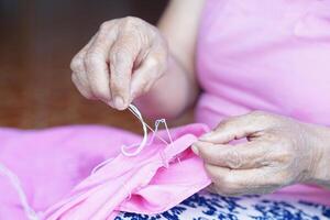 cerca arriba mayor mujer manos usos aguja y hilo a reparar ropa. concepto, pasatiempo, gratis hora actividad. bricolaje artesanía. reparar y mantenimiento ropa por mano. de coser. actividad a hogar para mayor foto