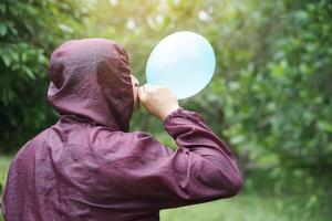 Asian man is blowing, inflating air into a balloon in the park. Concept, prepare balloon for playing games as a toy, decorate party or celebration. Recreation or leisure activity. Fun and happy time. photo