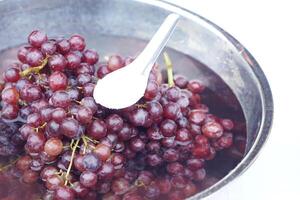 Soak grape fruits in water, spoon of baking soda powder. Concept, cleaning fruits. How to wash grapes for cleanliness and safety before eating. Wash and soak in baking soda water at least 20 minutes. photo