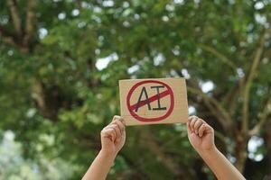 Close up hand holds paper card with No AI,  prohibition sign, outdoor nature background. Concept, disagree, anti or don't support  or not allow to use AI or Artificial Intelligence in daily life. photo