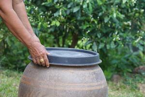 Closeup hands hold lid to cover water jar to protect from mosquitoes to breed inside or other  insects or dust go into water. Concept, campaign to stop mosquitoes cycle to lay eggs in water container photo