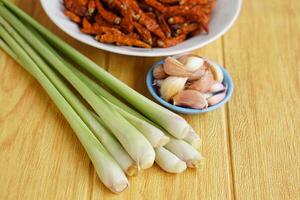 Fresh lemongrass, bowls of garlic and dried chillies on brown wooden floor. Concept, food ingredients, prepared for cooking. Herbal plants in Thai kitchen for various menus. photo