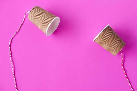 DIY paper cups with string on pink background. Concept, telephone toys which apply with science knowledge about vibration sound through straining strings causing us to hear the sound. photo