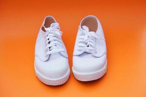 Pair of new white canvas sneakers,  Orange background. Comfortable, fashionable style. Concept, shoes for doing sport or exercise also can wear for traveling, hiking or doing active activity. photo