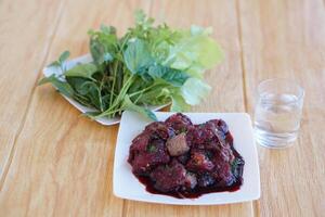 White plate of  traditional local food, sliced fresh raw beef to small pieces, mixed with Thai herbs ingredients and blood, plate of vegetables. Concept, weird food. photo