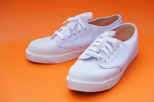 Pair of new white canvas sneakers,  Orange background. Comfortable, fashionable style. Concept, shoes for doing sport or exercise also can wear for traveling, hiking or doing active activity. photo