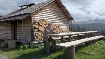 een Mens is resting in de buurt een oud houten huis in de bergen. de echt huis van Karpaten herders in de bergen. concept van avontuur, reizen en ontsnappen van de stad. langzaam beweging beeldmateriaal 4k video