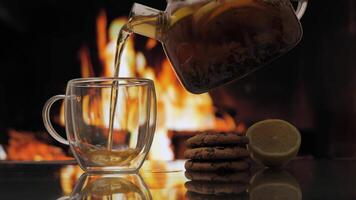 Pouring fruit tea in cup against background of a fireplace with a flame. Fresh hot herbal tea with mint and oranges, detox drink. video