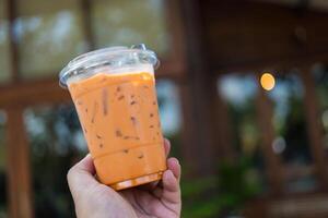 Man holding a plastic cup of iced Thai milk tea photo