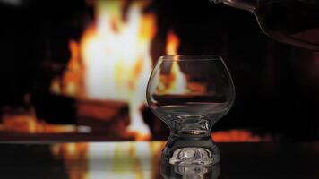 gieten whisky of cognac van een fles naar een glas over- haard achtergrond. warmte en huis comfort. 4k video