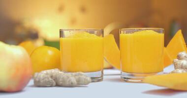 Orange smoothies in glasses on a background of fresh vegetables and fruits. The fresh cocktail is ready to eat. Healthy and vegetarian food concept. Ultra 4K Close-up video