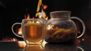 tetera y vaso con Fruta té en contra antecedentes de un hogar con un fuego. Fresco caliente herbario té con menta y naranjas, desintoxicación beber. video