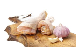 Raw uncooked chicken legs with garlic, drumsticks on wooden board. photo