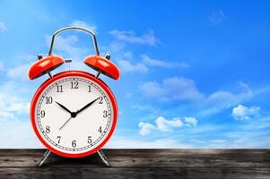 Vintage red alarm clock on wooden table on blue sky photo