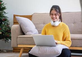 Beautiful young woman in a yellow casual dress enjoying listening to music and smiling while relaxing on the sofa at home. Young woman with headphones uses laptop and smartphone at home. relax concept photo