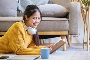 Beautiful young woman in a yellow casual dress enjoying listening to music and smiling while relaxing on the sofa at home. Young woman with headphones uses laptop and smartphone at home. relax concept photo