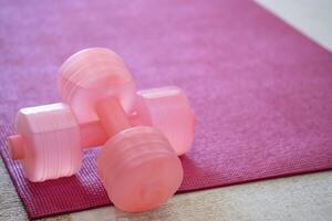 A pink yoga mat with two pink colored dumbbells on it. Fitness equipment for home exercise and flexibility training. photo