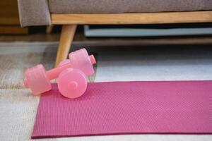 A pink yoga mat with two pink colored dumbbells on it. Fitness equipment for home exercise and flexibility training. photo