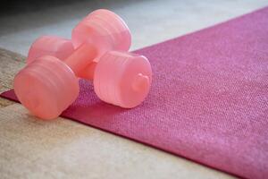 A pink yoga mat with two pink colored dumbbells on it. Fitness equipment for home exercise and flexibility training. photo