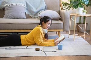 Beautiful young woman in a yellow casual dress enjoying listening to music and smiling while relaxing on the sofa at home. Young woman with headphones uses laptop and smartphone at home. relax concept photo
