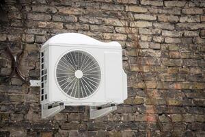 White air conditioner hanging on a dark brown old building brick wall of covered in snow photo