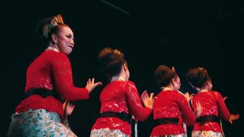 traditionnel danseurs dans rouge costumes performant sur étape avec joyeux expressions, projecteur dans le Contexte. video