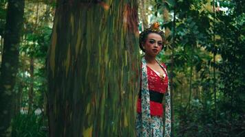 Enigmatic woman in vibrant red attire posing in a lush forest, exuding a sense of mystery and connection with nature. video