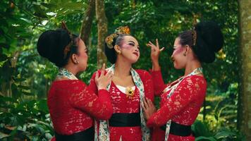 Three women in traditional Balinese attire posing in a tropical setting. video