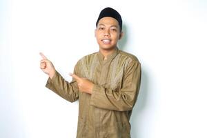 smiling asian muslim man pointing to the right side wearing islamic dress isolated on white background photo