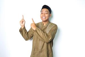 smiling asian muslim man wearing koko clothes pointing to above with excitement expression looking at camera isolated on white background photo