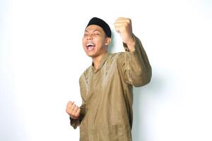 excited asian muslim man wearing islamic clothes raising fist showing victory gesture in eid mubarak celebration isolated on white gesture photo