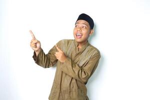 surprised asian muslim man wearing islamic clothes pointing to above and looking up isolated in white background photo