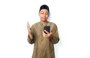 calm asian moslem man raising hand to praying when read message using mobile phone isolated on white background photo