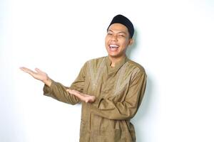 ecstatic asian moslem man wearing islamic dress raising palm to the right side to presenting with laughing expression isolated on whiote background photo