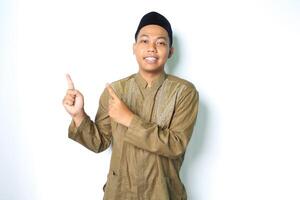 smiling asian muslim man pointing to above wearing islamic dress isolated on white background photo