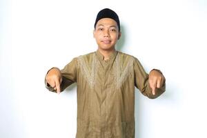calm asian muslim man smiling at camera wearing koko clothes pointing down isolated on white background photo