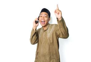 excited asian muslim male pointing above while talking using mobile phone isolated on white background photo