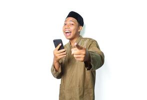 funny asian muslim man screaming while pointing at camera with holding moblie phone isolated on white background photo