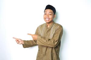 smiling asian muslim man wearing koko clothes pointing to beside with excitement expression looking at camera isolated on white background photo