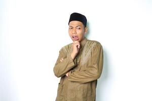 thoughtful asian muslim man thinking seriously with hand on chin wearing koko clothes isolated on white background photo