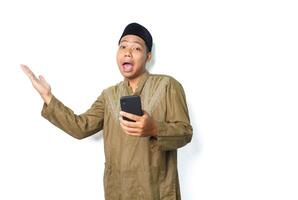 funny asian muslim man presenting copy space with holding mobile phone isolated on white background, looking at camera photo